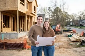 Jeune couple souriant devant une maison en construction